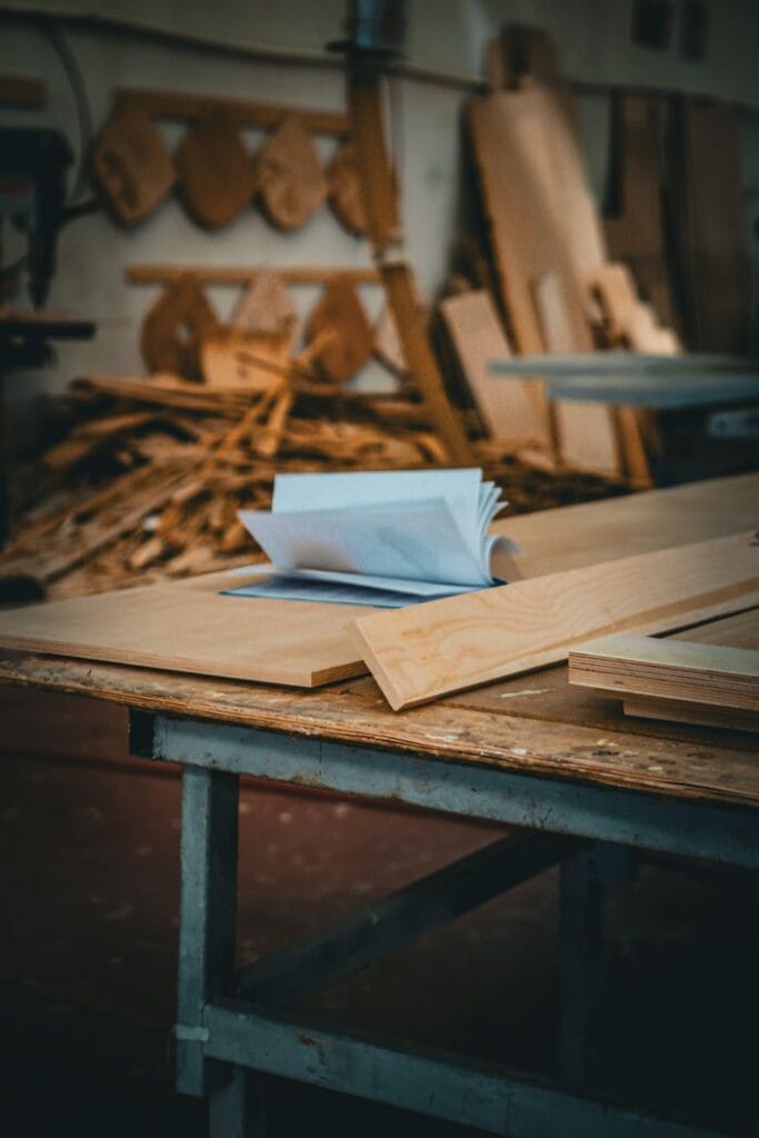 A detailed view of a carpentry table inside a workshop with stacks of wood and tools in the background.