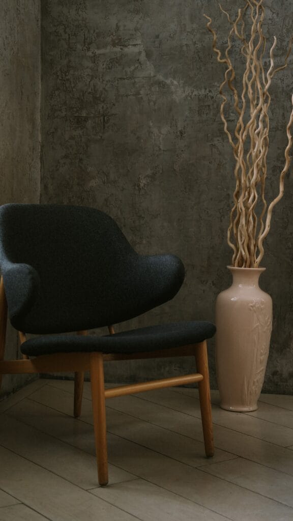 A mid-century modern chair beside a decorative vase in a minimalistic indoor setting.