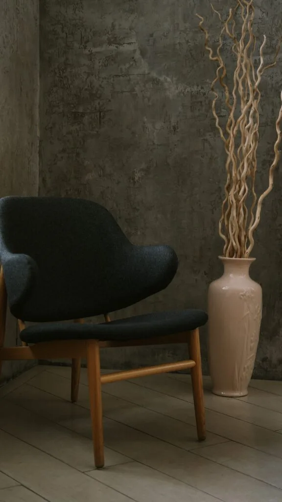 A mid-century modern chair beside a decorative vase in a minimalistic indoor setting.