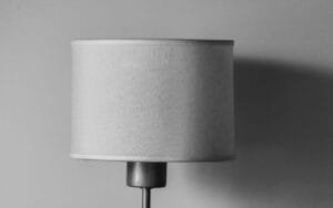 A black and white photo featuring a minimalist lamp with a fabric shade casting a shadow on the wall.