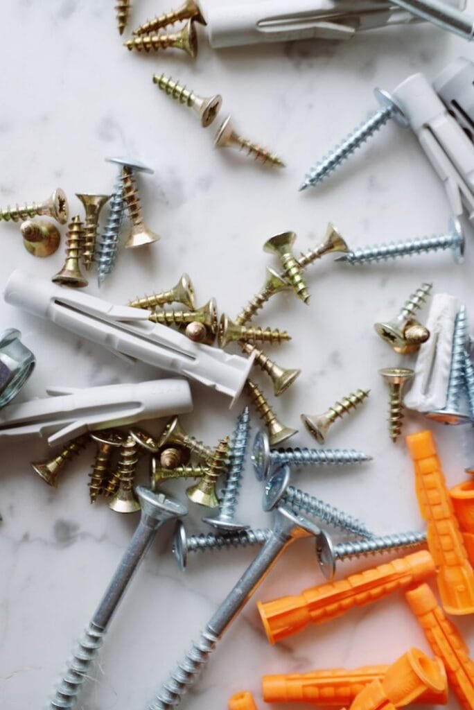 Bunch of various multicolored plastic dowels and metal screws placed on white marble table in modern workshop