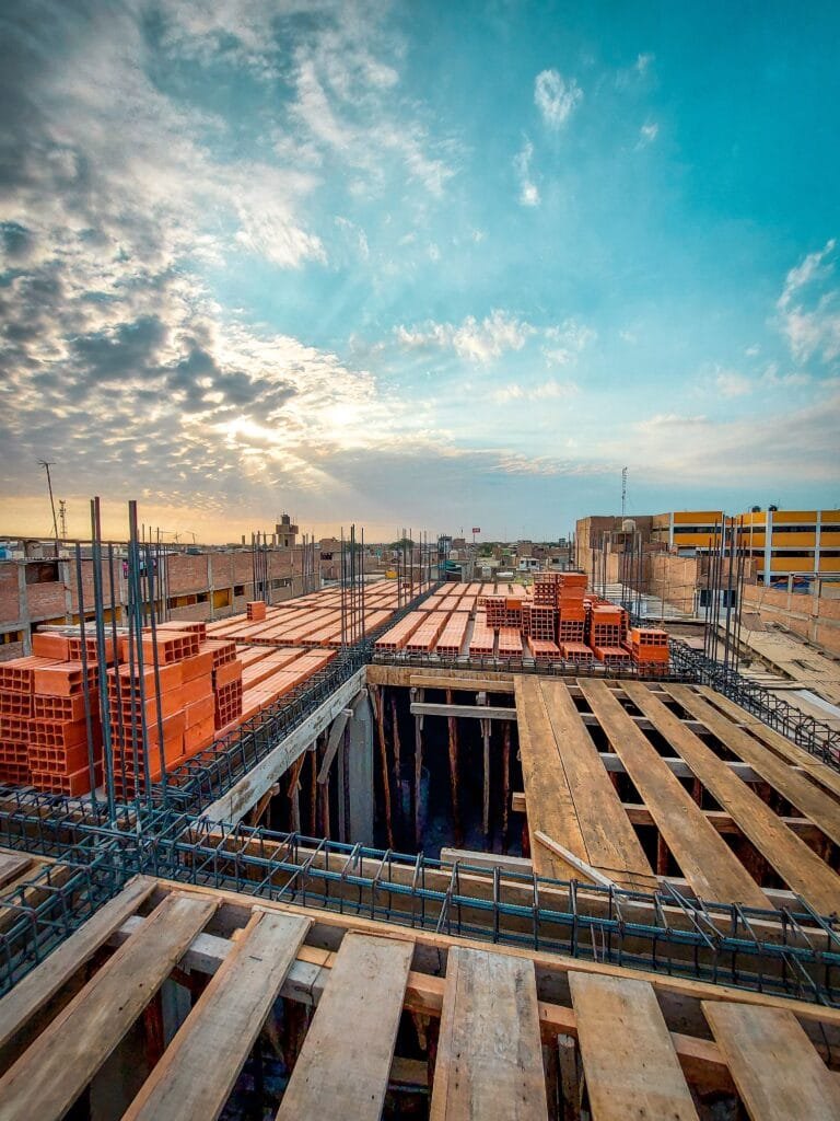 Bird's-eye view of an industrial construction site with stacks of red bricks and wooden planks under a blue sky at sunrise.